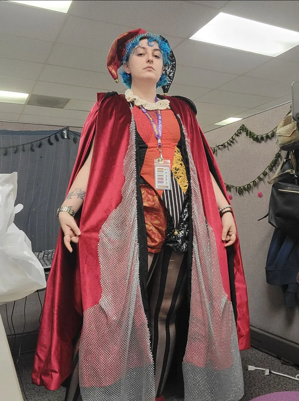 someone wearing a red and black jester costume with a long red velvet cloak over it.