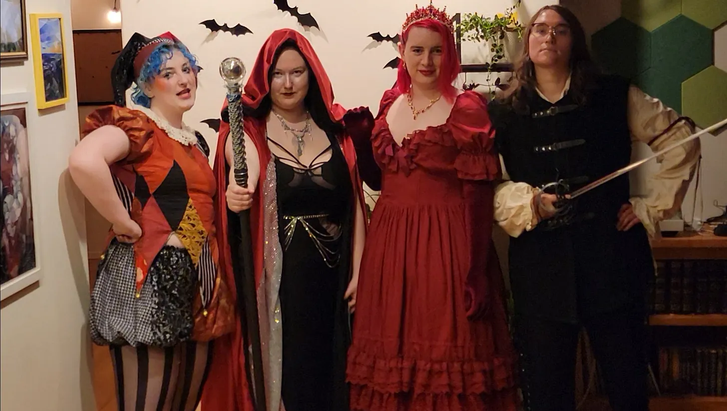 A group of people in elaborate costumes. From left to right they are dressed as a jester, a sorcerer in a long cloak, a princess, and a knight.